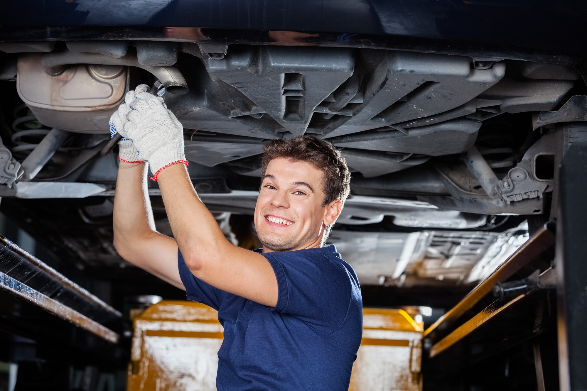 Smiling Mechanic Working Underneath Lifted Car